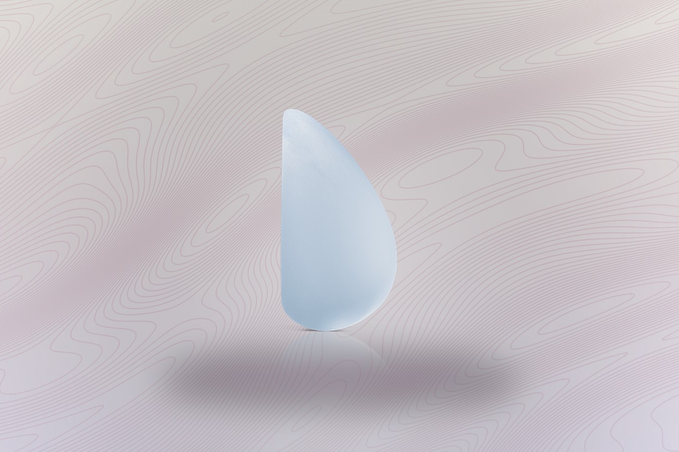 Motiva Ergonomix breast implant, the teardrop silhouette it takes when upright, on a soft wave background.